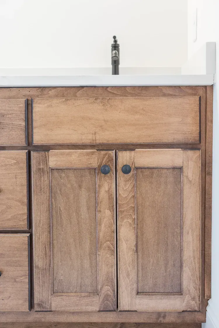 Wooden bathroom vanity with cabinet doors and sink countertop in front of a white wall.