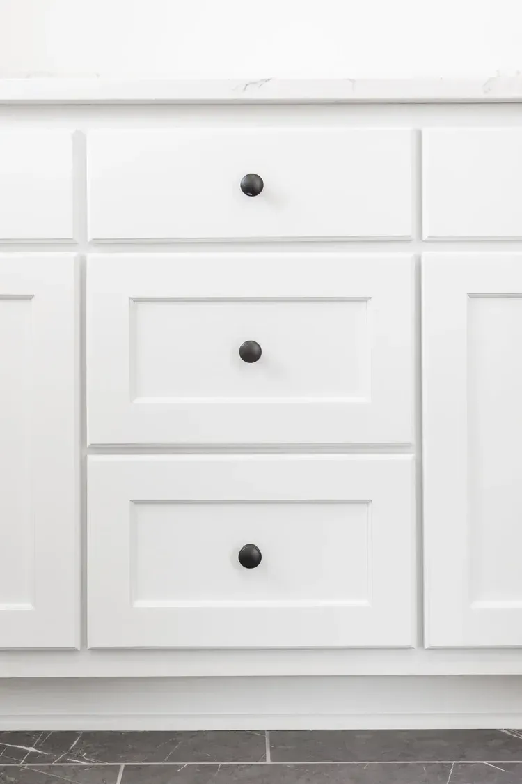 White kitchen cabinets with black knobs and a dark tile floor