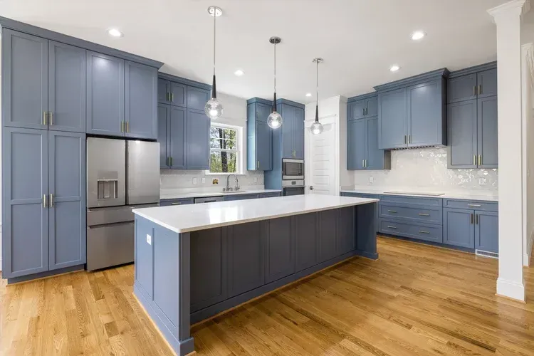 Bright modern kitchen with blue cabinets, white island, stainless steel appliances, and hardwood floors