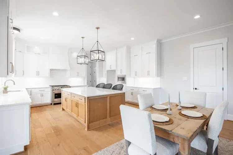 Bright white kitchen and dining area with a wooden table, island, and pendant lights