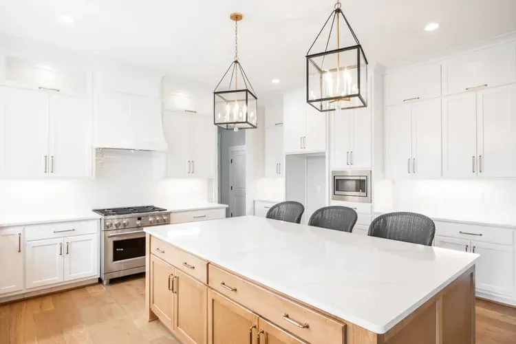 Bright white modern kitchen with island, wood cabinets, black chairs, and hanging pendant lights