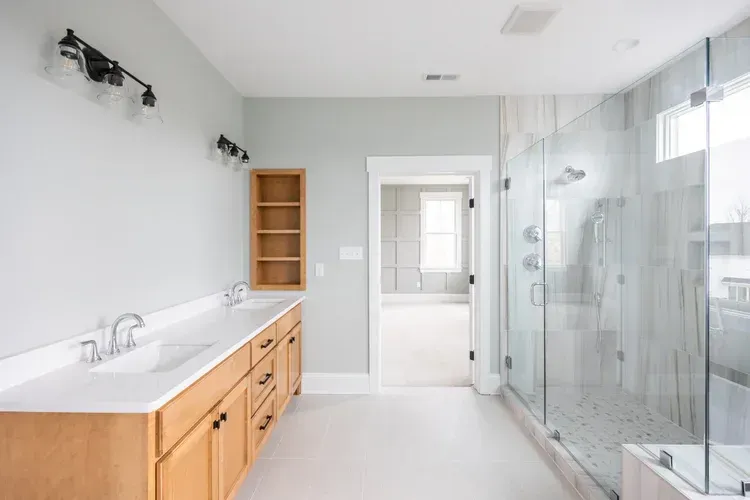 Bright modern bathroom with double sink vanity, glass shower, and white tile walls