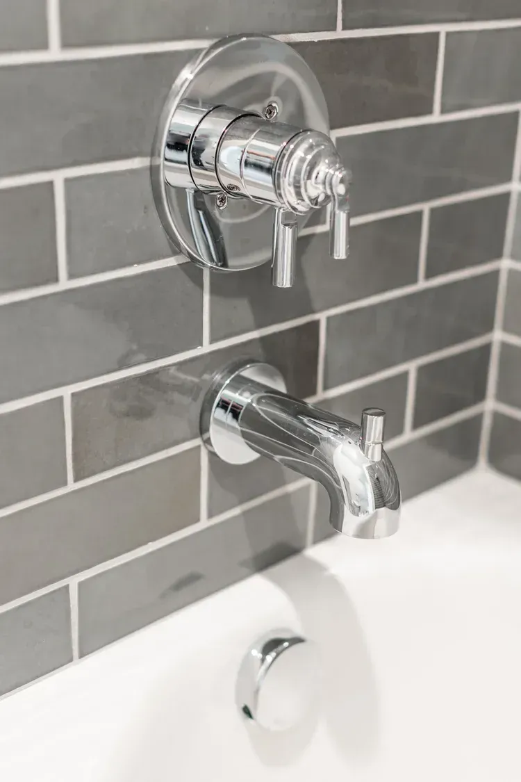 Chrome bathtub faucet and control on gray tiled bathroom wall