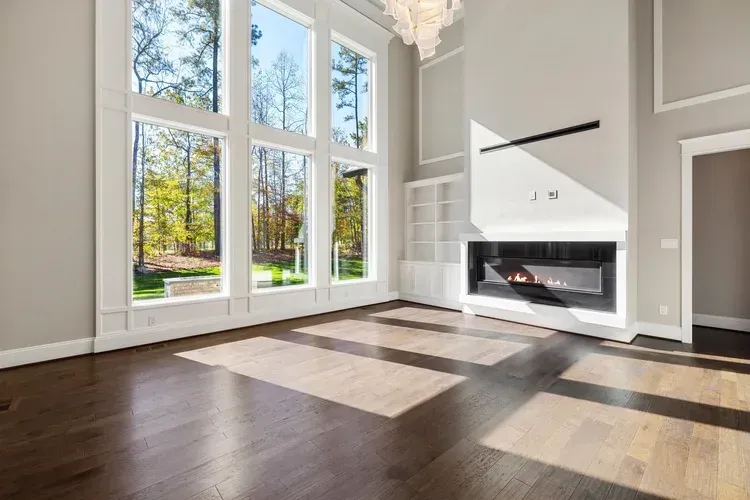 Bright modern living room with tall windows, dark wood floors, and a white fireplace.