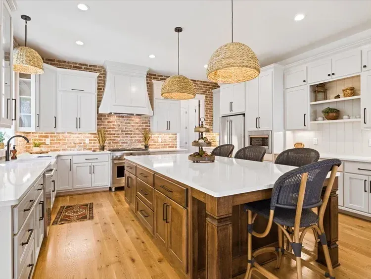 Bright modern kitchen with white cabinets, wood floor, large island, and wicker pendant lights