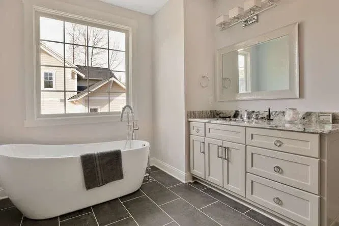 Modern bathroom with white soaking tub, gray tile floor, and vanity with mirror.