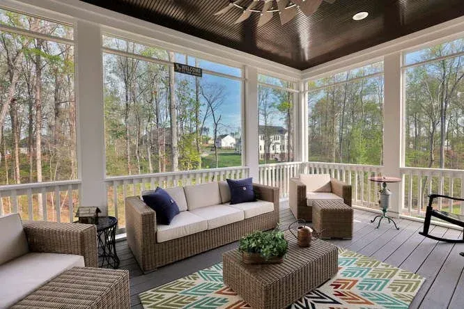 Covered porch with wicker furniture, patterned rug, and trees visible through large windows.