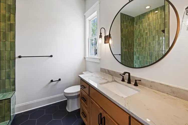 Modern bathroom with double sink vanity, round mirror, toilet, and black hex tile floor