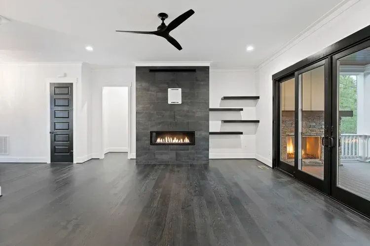 Modern living room with dark floors, black fireplace wall, ceiling fan, and large sliding glass doors