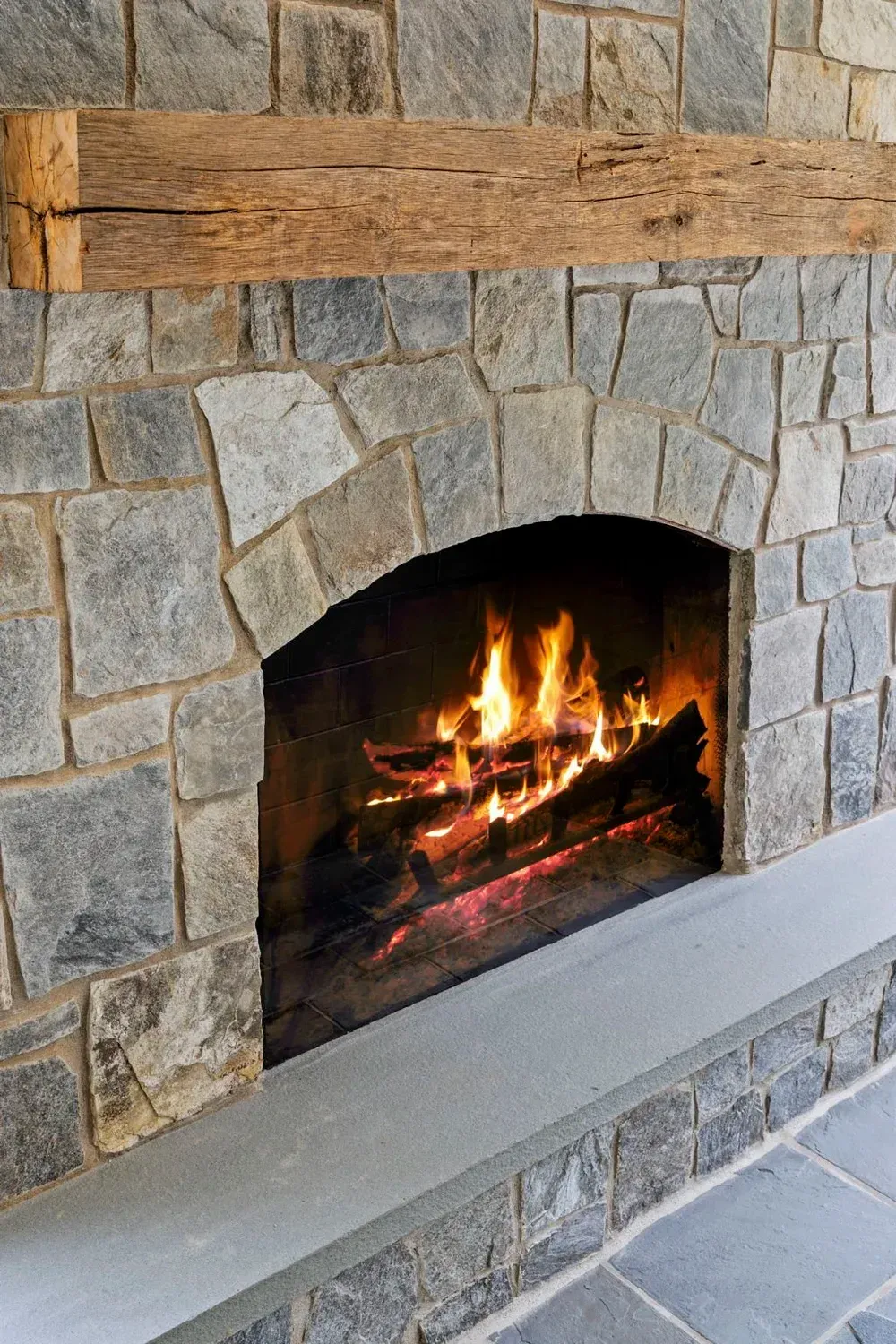 Stone fireplace with a burning fire and rustic wooden mantel