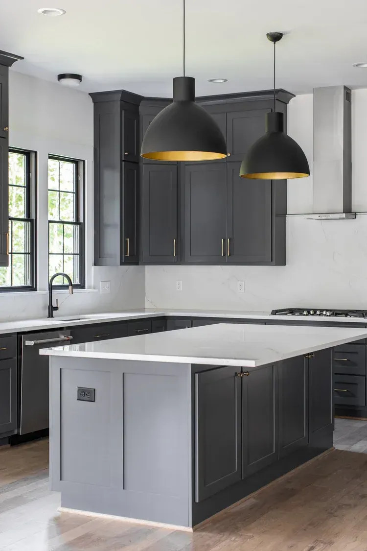 Modern kitchen with dark cabinets, white island, black pendant lights, and wood flooring