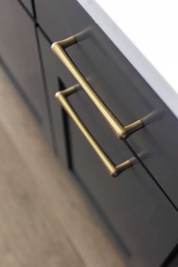 Close-up of a dark cabinet with brass bar handles and a wood floor beside it