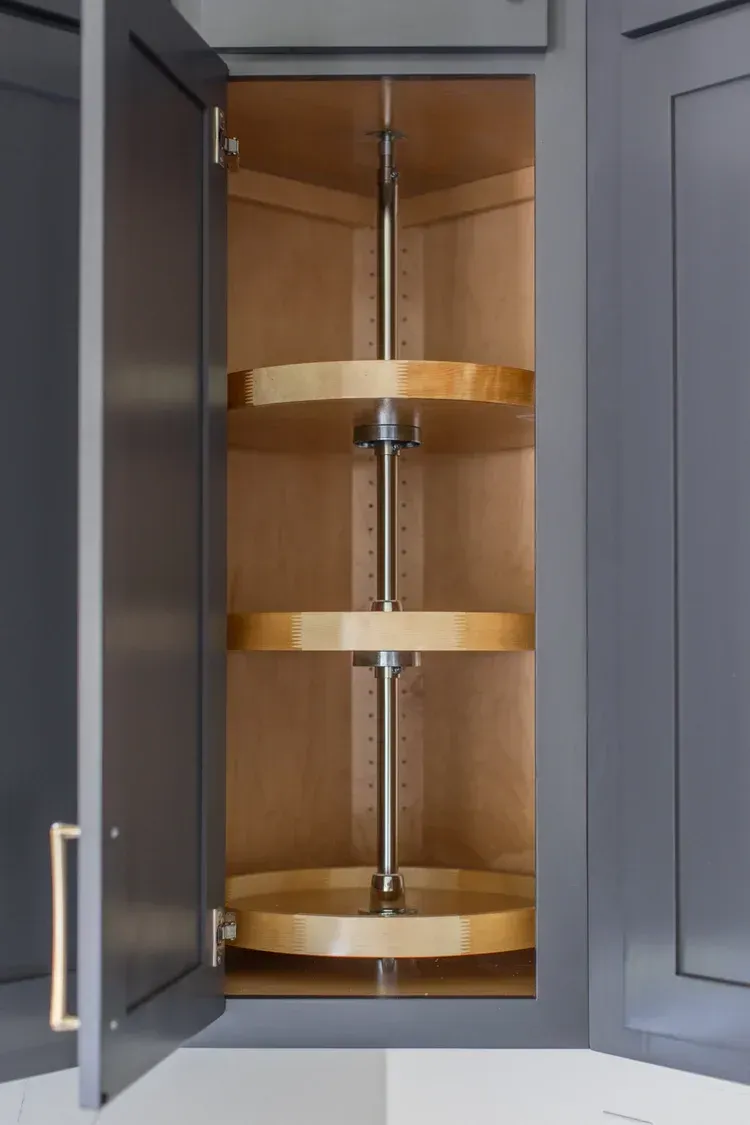 Open cabinet with pull-out wooden lazy Susan shelves in a gray kitchen cabinet