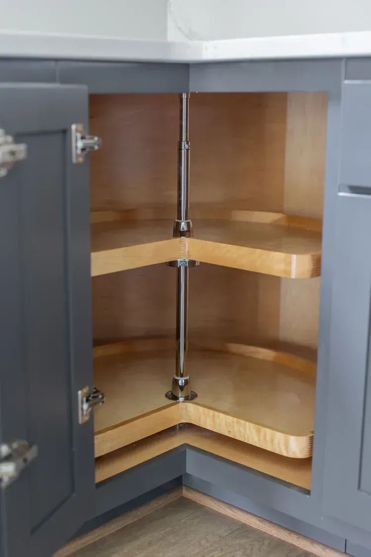 Open corner cabinet with empty wooden shelves and silver hinges in a gray kitchen.