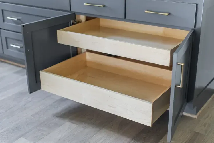 Open kitchen drawers with light wood interiors in dark gray cabinets