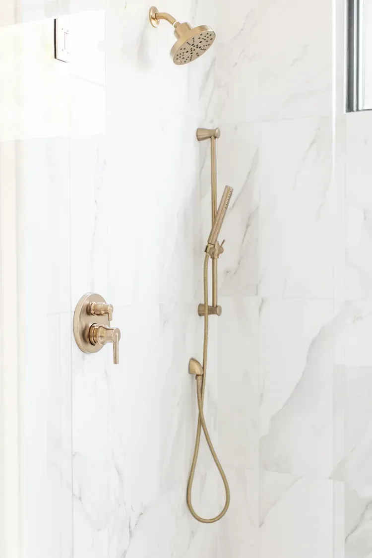 Gold shower fixtures on a white marble-tile bathroom wall