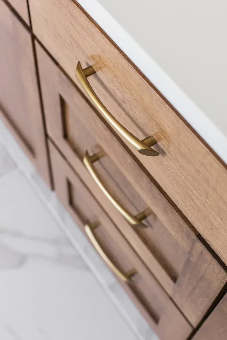 Close-up of wood cabinet drawers with curved gold handles and white countertop edge