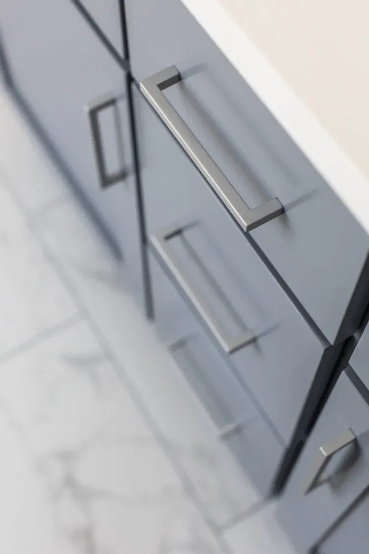 Gray kitchen cabinets with long metal handles on a light tiled floor.