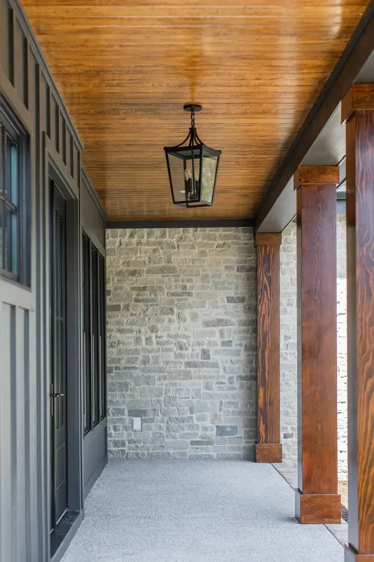 Covered porch with wood ceiling, hanging lantern, stone wall, and dark-framed windows and columns