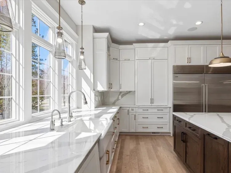 Bright white modern kitchen with large windows, marble counters, and stainless steel appliances