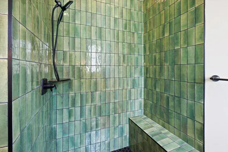 Green-tiled shower with black showerhead and bench, viewed from inside the stall