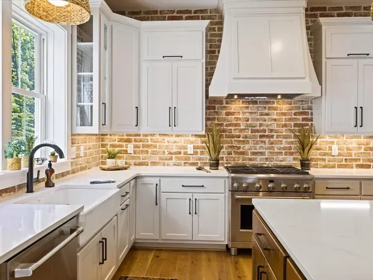 Bright kitchen with white cabinets, brick backsplash, and a central island under warm lighting