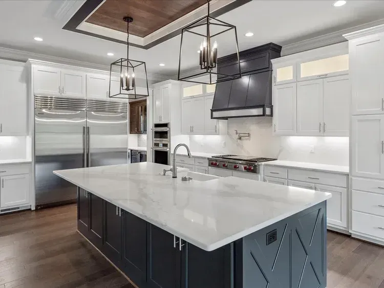 Modern white kitchen with stainless steel appliances, marble island, and dark wood ceiling accents
