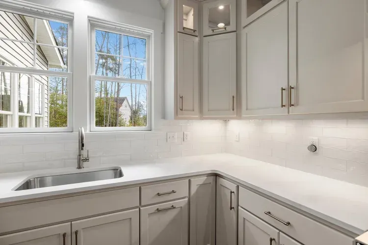 Bright white kitchen with corner sink, large windows, and light gray cabinets