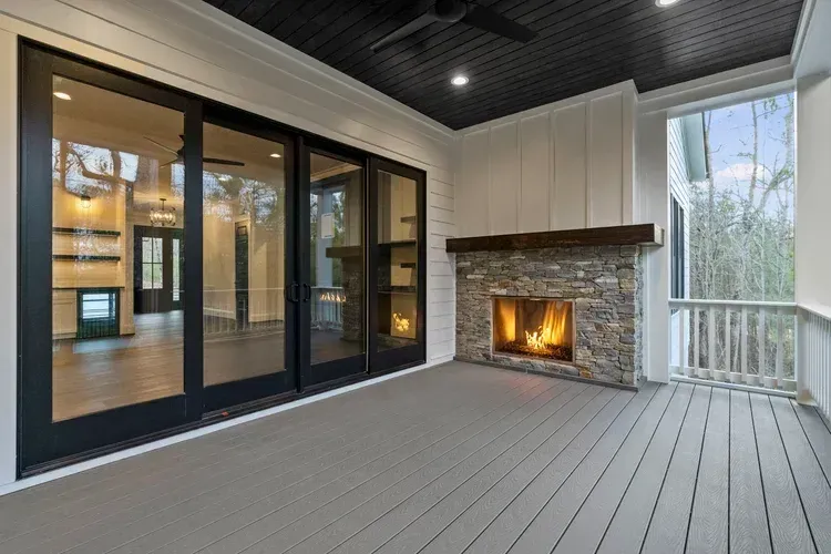 Covered patio with gray deck, black sliding doors, and a lit stone fireplace.
