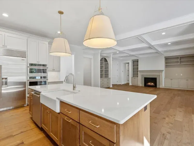 Bright modern kitchen with white island, pendant lights, hardwood floors, and open living area with fireplace