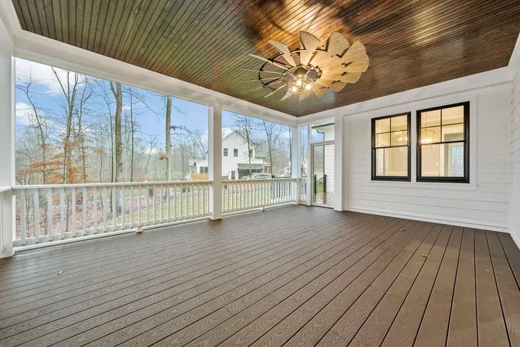 Covered porch with wood-look flooring, white railing, windows, and a ceiling fan under a dark wood ceiling.