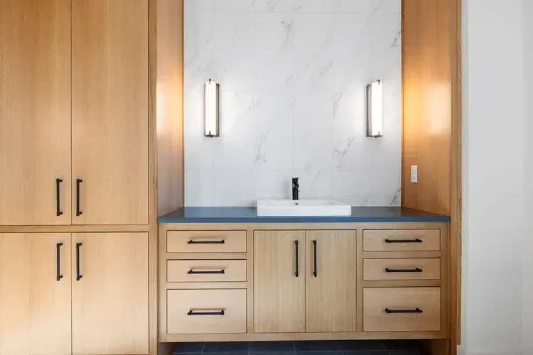 Modern bathroom vanity with light wood cabinets, white countertop, and twin wall sconces
