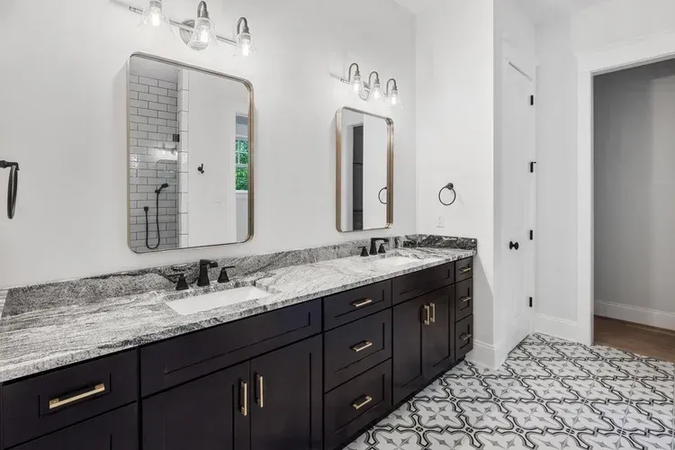 Modern bathroom with double vanity, black cabinets, marble countertop, mirrors, and patterned tile floor.