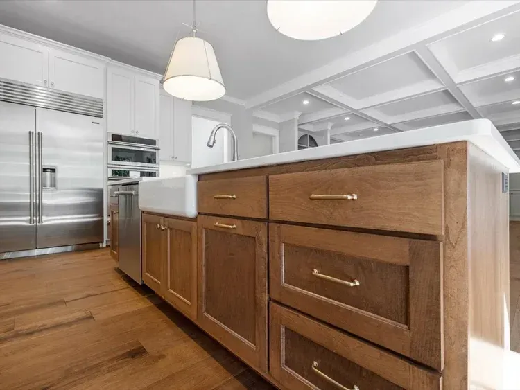 Modern kitchen with wood island drawers, stainless steel appliances, and white pendant lights