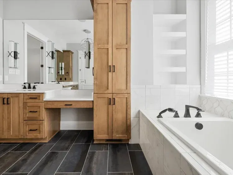Modern bathroom with wood vanity, large mirror, and white tub beside a window.