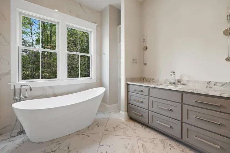 Bright modern bathroom with freestanding tub, double vanity, marble floors, and large windows