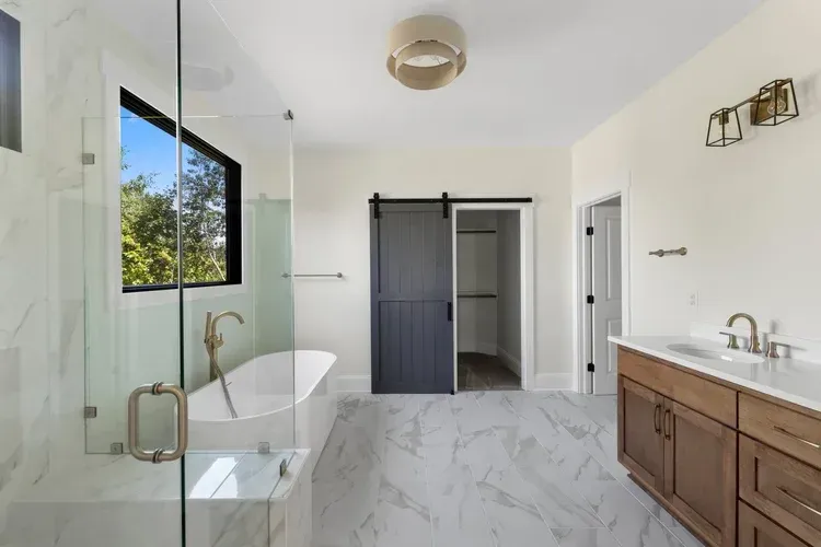 Bright modern bathroom with freestanding tub, glass shower, wood vanity, and sliding barn door