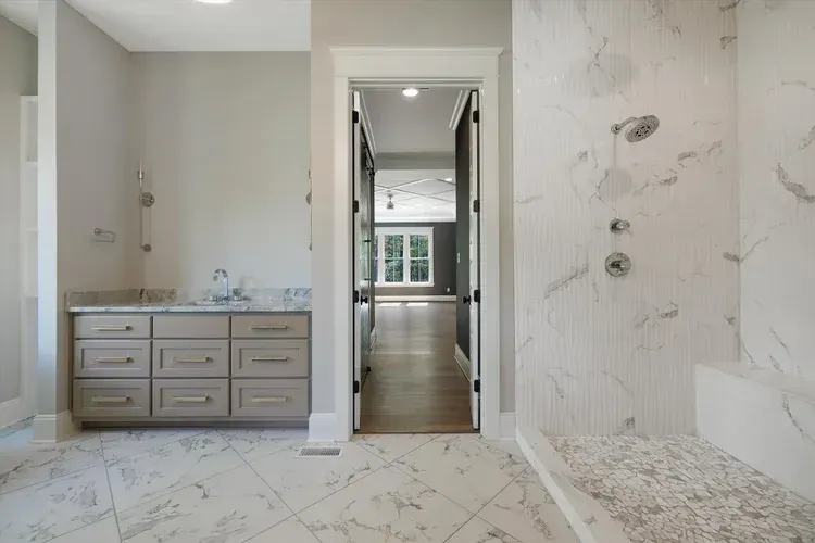 Modern marble bathroom with double vanity, walk-in shower, and mirrored doorway to a bright hallway