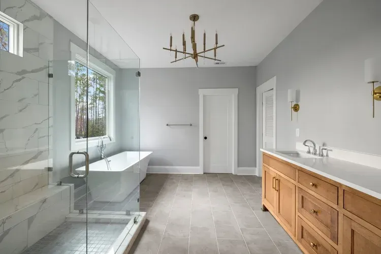 Bright modern bathroom with glass shower, freestanding tub, and wood vanity under a chandelier