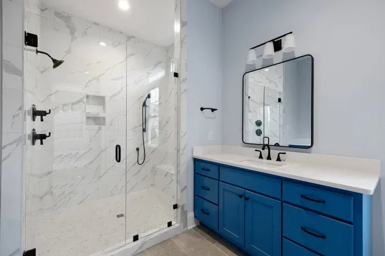 Modern bathroom with glass shower, blue vanity, white countertop, and black fixtures