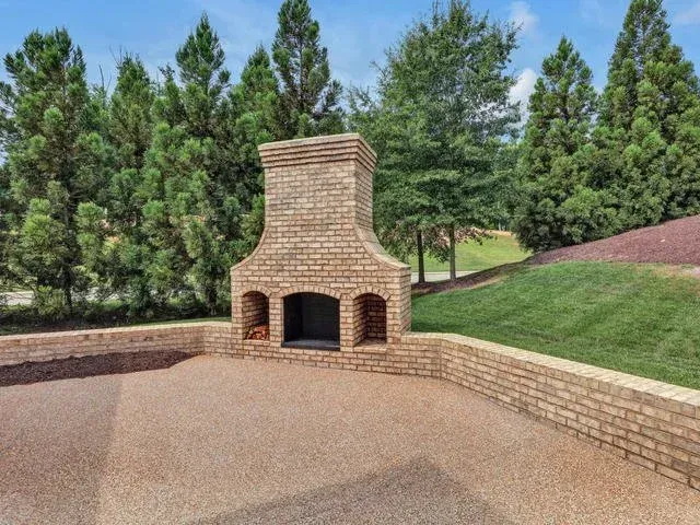 Brick outdoor fireplace with arched openings beside a paved patio and green lawn under trees