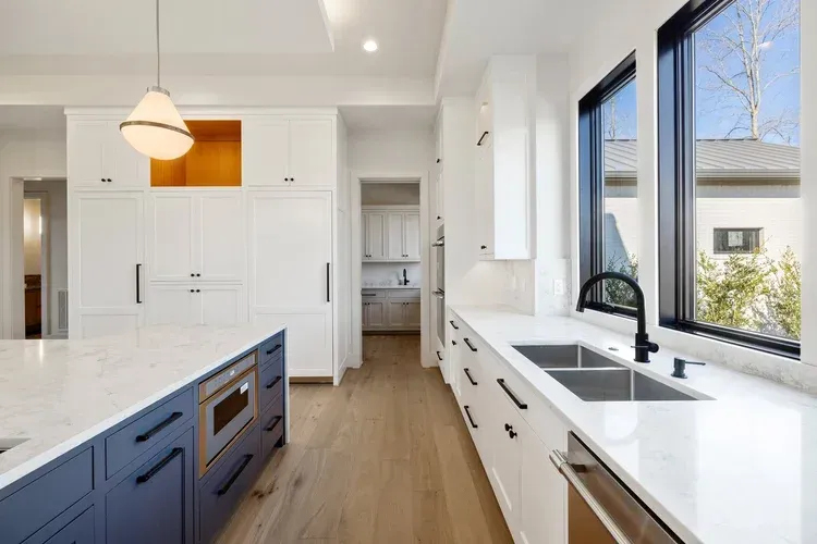 Bright modern kitchen with white cabinets, blue island, wood floors, and large windows overlooking outdoors