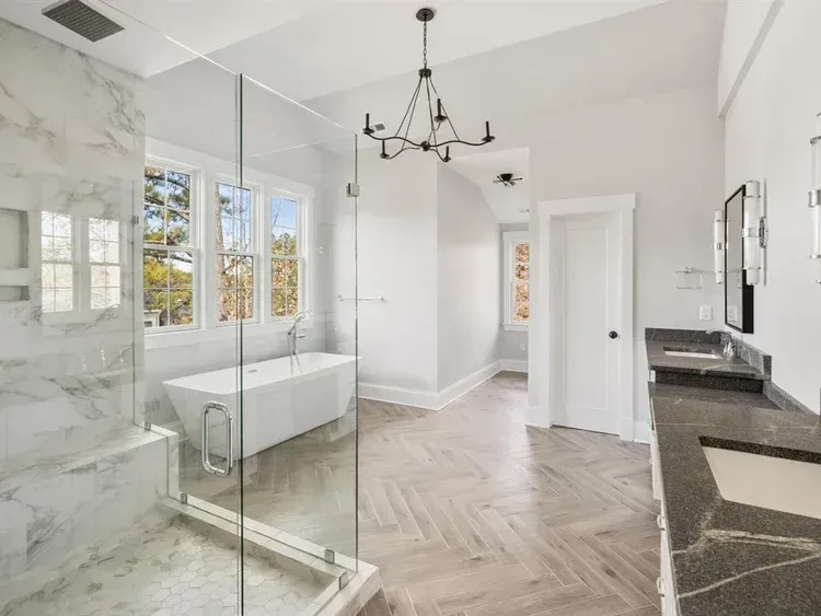Bright modern bathroom with glass shower, freestanding tub, marble walls, and herringbone tile floor