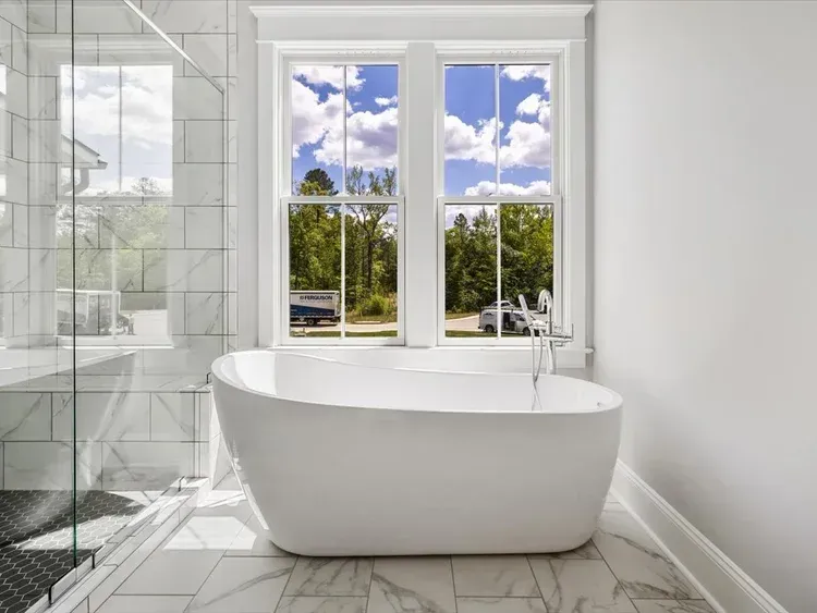Bright bathroom with a white freestanding tub beside a glass shower and large windows overlooking greenery