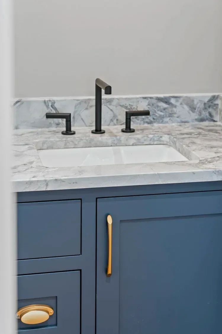 Blue bathroom vanity with marble countertop, white sink, and matte black faucet and handles