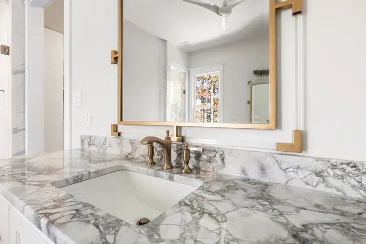 Marble bathroom vanity with gold-framed mirror and sink in a bright, modern interior