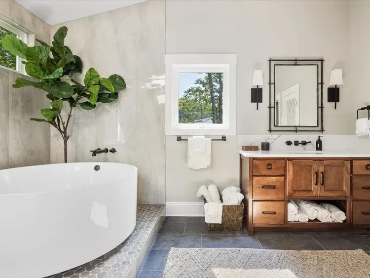 Modern bathroom with a freestanding tub, vanity, mirror, and potted plant by a window.