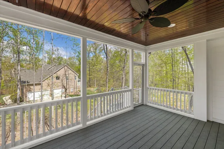 Covered screened porch with gray floor, white railings, and wooded view outside