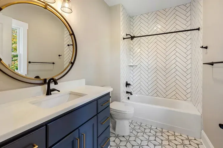 Modern bathroom with navy vanity, round mirror, white sink, and herringbone tile shower surround