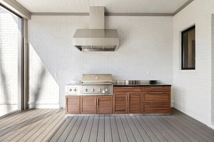 Modern outdoor kitchen with grill and wooden cabinets on a covered patio.